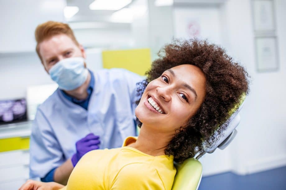 a woman smiling in a dental chair with a dentist in the background
